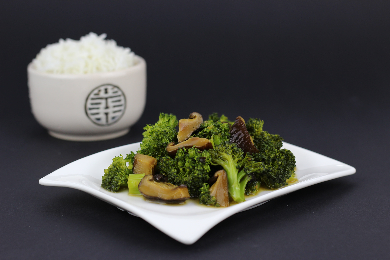 Garlic sautéed broccolini with mushrooms, served on a white plate with a bowl of steamed rice.
